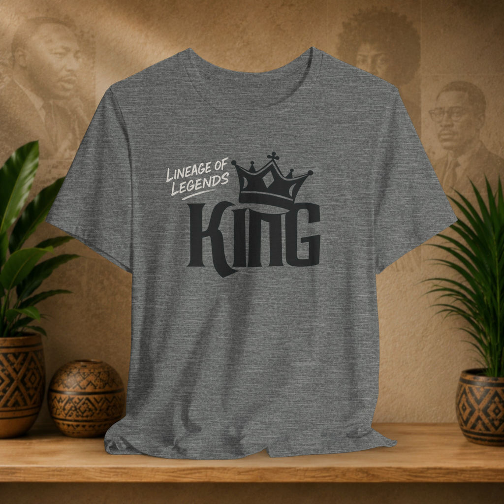 Light grey Lineage of Legends King graphic tee with black crown design, displayed on a shelf with plants and Afrocentric portraits