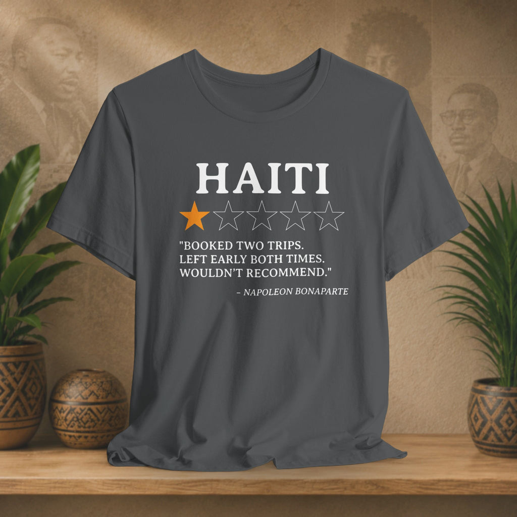 Gray t-shirt with Haiti-themed text and rating on a wooden surface with plants and decorative items.