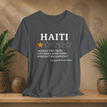 Gray t-shirt with Haiti-themed text and rating on a wooden surface with plants and decorative items.