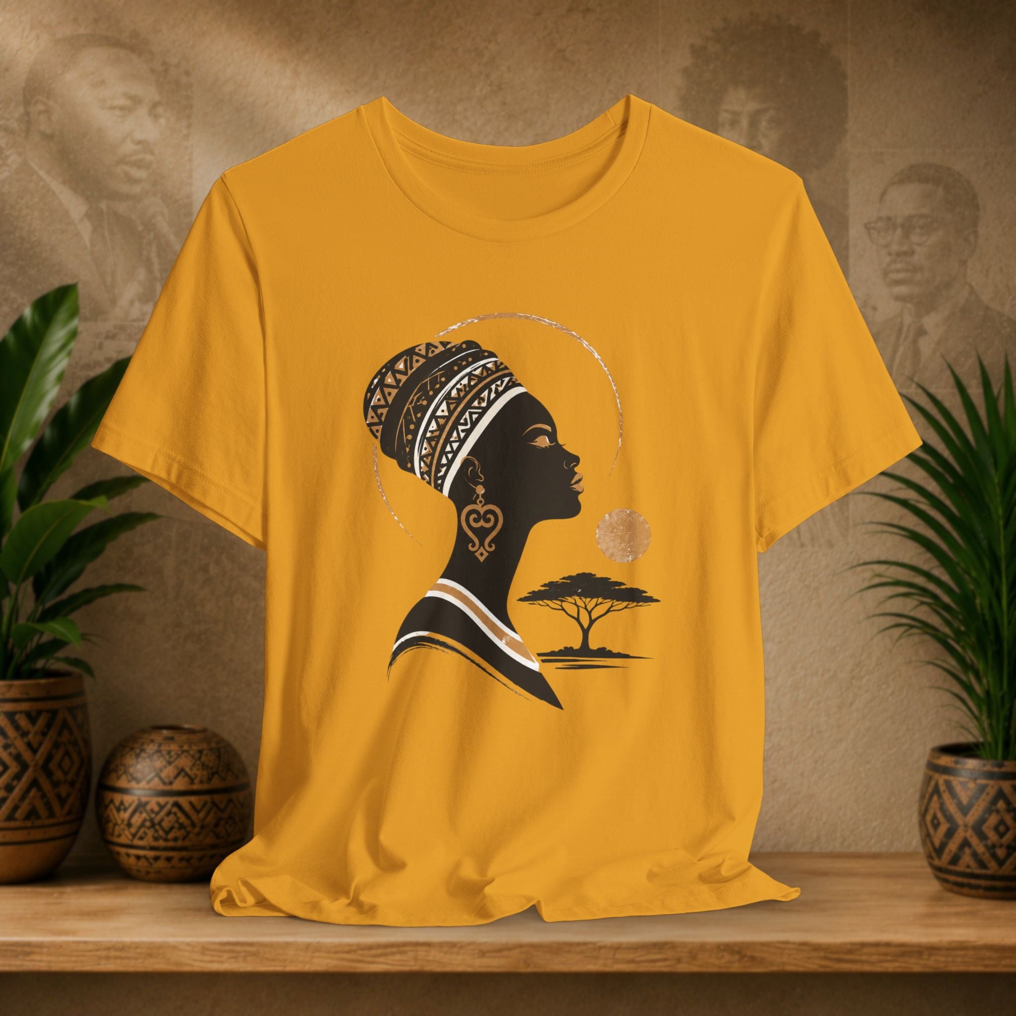 Yellow t-shirt with a black silhouette of a woman with an afro and a tree design on a wooden surface with plants and decorative items.