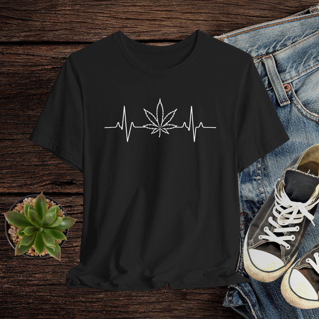 Black t-shirt with a cannabis leaf and heartbeat line design on a wooden surface with jeans and sneakers.