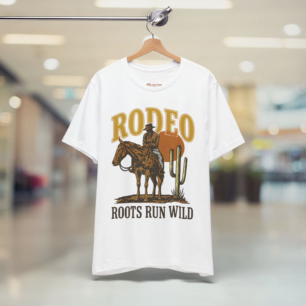 White t-shirt with a cowboy graphic and 'Rodeo Roots Run Wild' text on a hanger in a store.