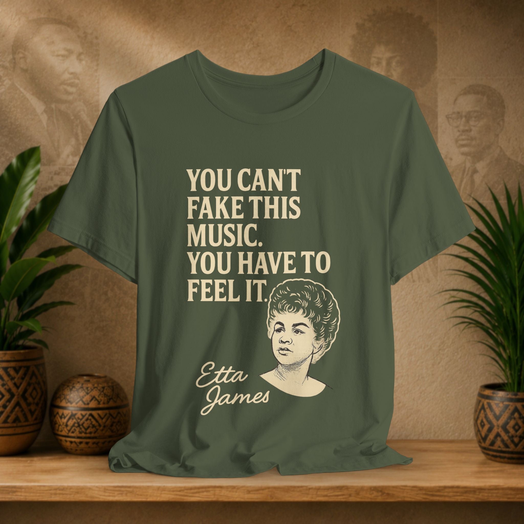 Green t-shirt with text and a portrait of Etta James on a wooden surface with plants and a vintage-style wall.