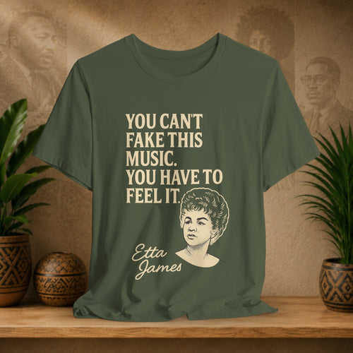 Green t-shirt with text and a portrait of Etta James on a wooden surface with plants and a vintage-style wall.
