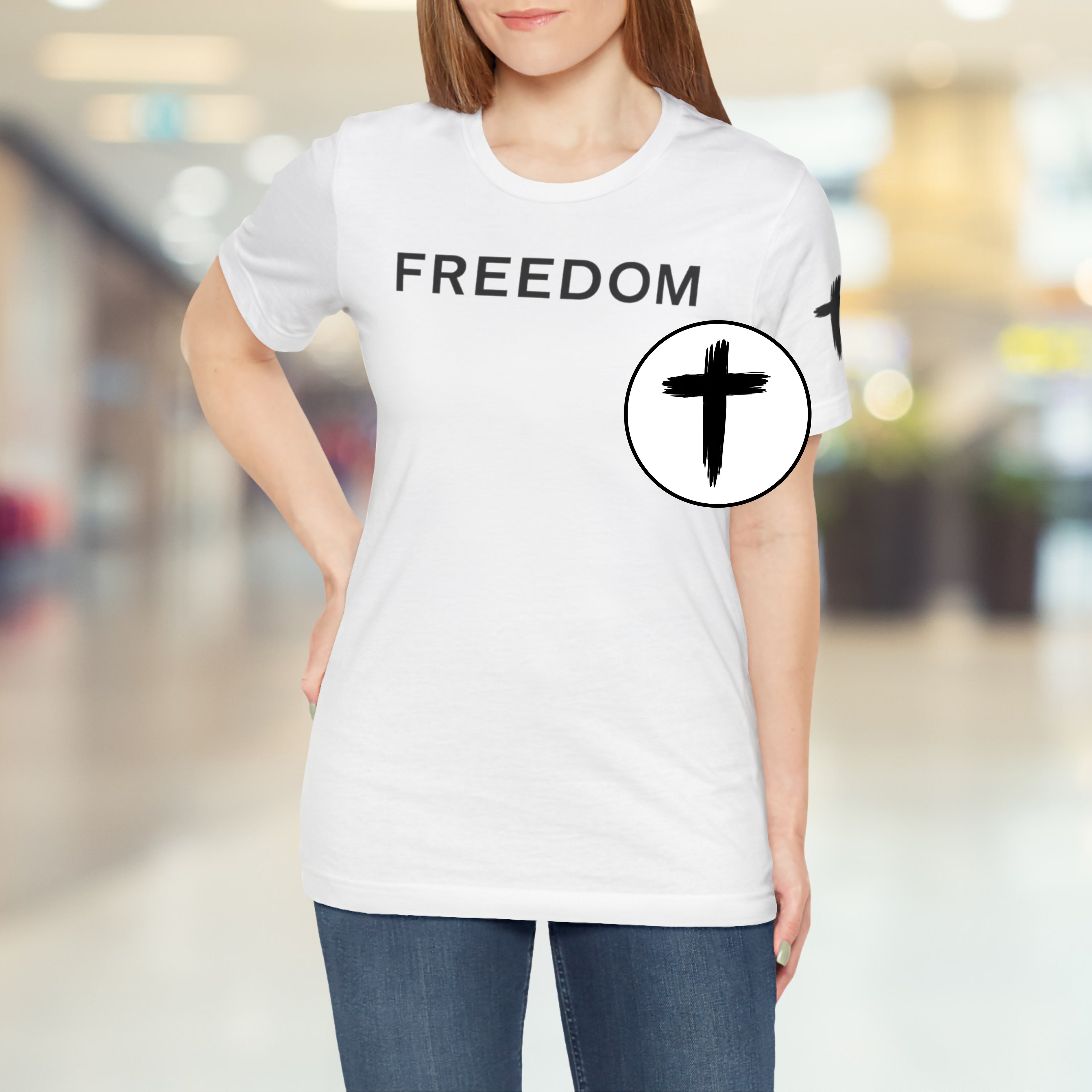 Person wearing a white t-shirt with 'FREEDOM' and a black circle design in a blurred indoor setting
